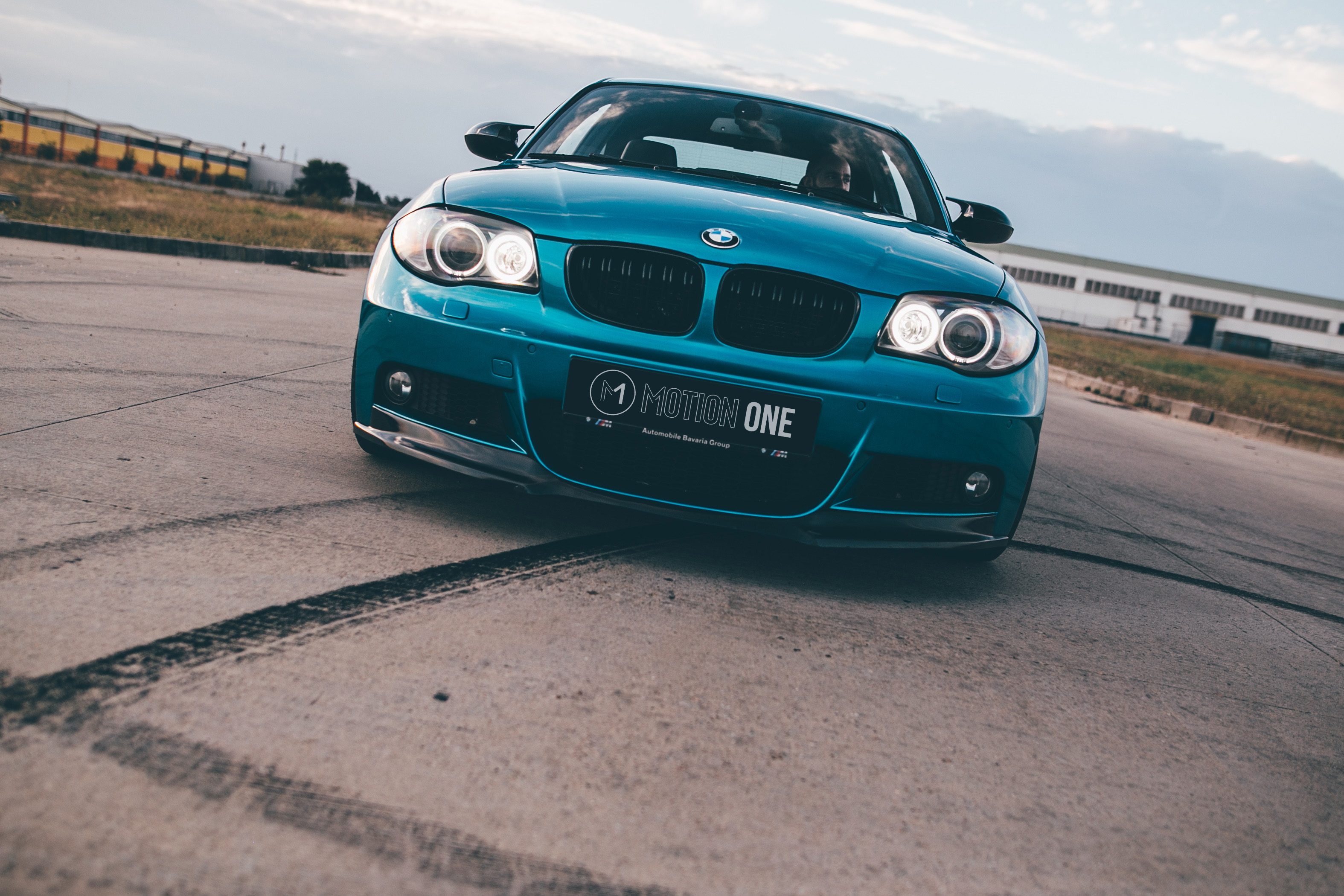 BMW teal, vedere frontală, faruri aprinse, pe asfalt
